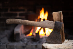 Annette's Wood-Fired Cuisine - an ax stuck in a wooden stump near a burning fireplace